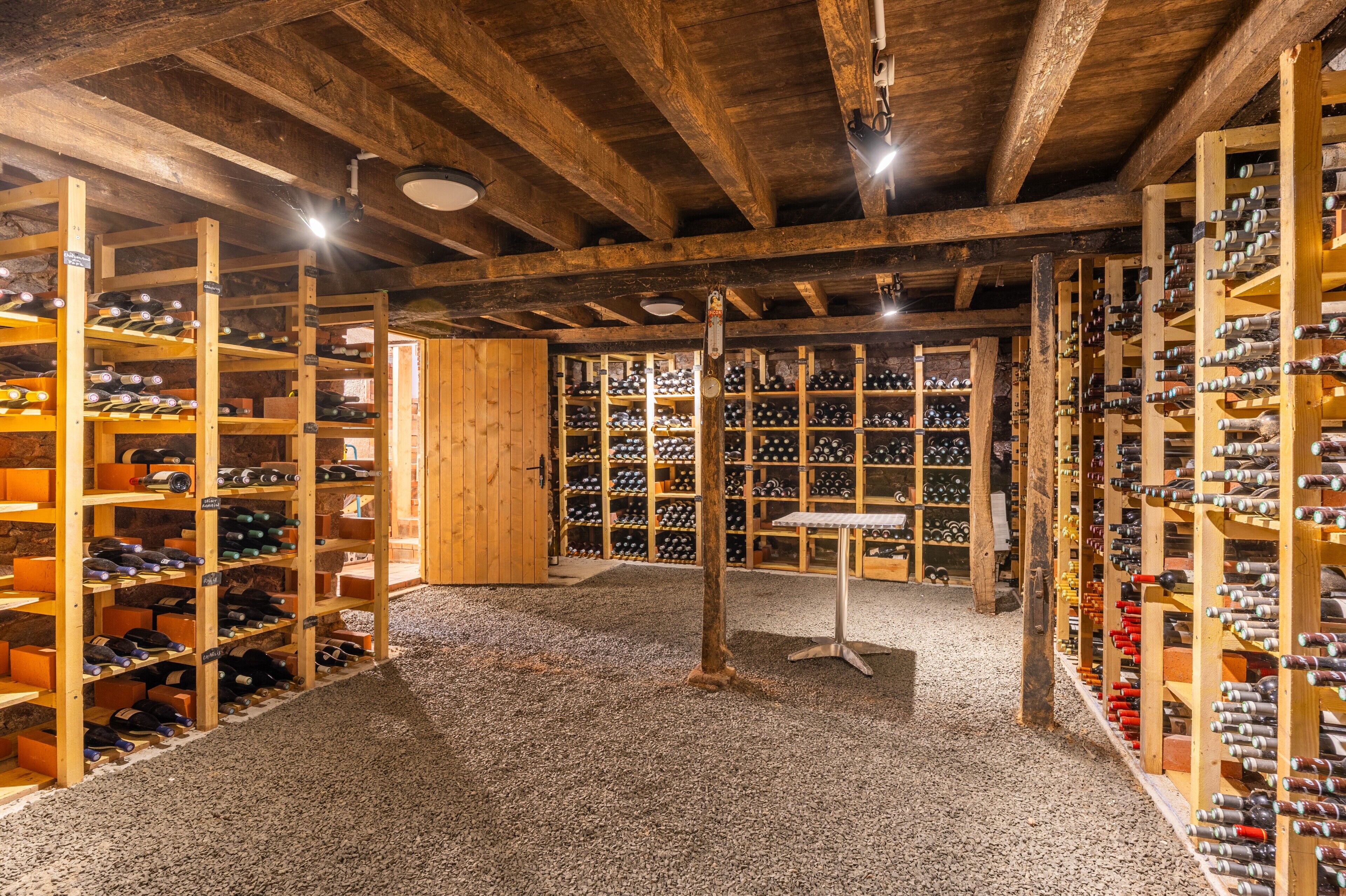A wine cellar with wooden racks and shelves, a gravel floor, and a wooden door.