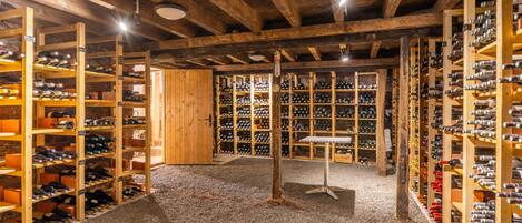 A wine cellar with wooden racks and shelves, a gravel floor, and a wooden door.