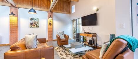 A modern living room with leather sofas, a glass coffee table, a fireplace, a television, and wooden beams on the ceiling.