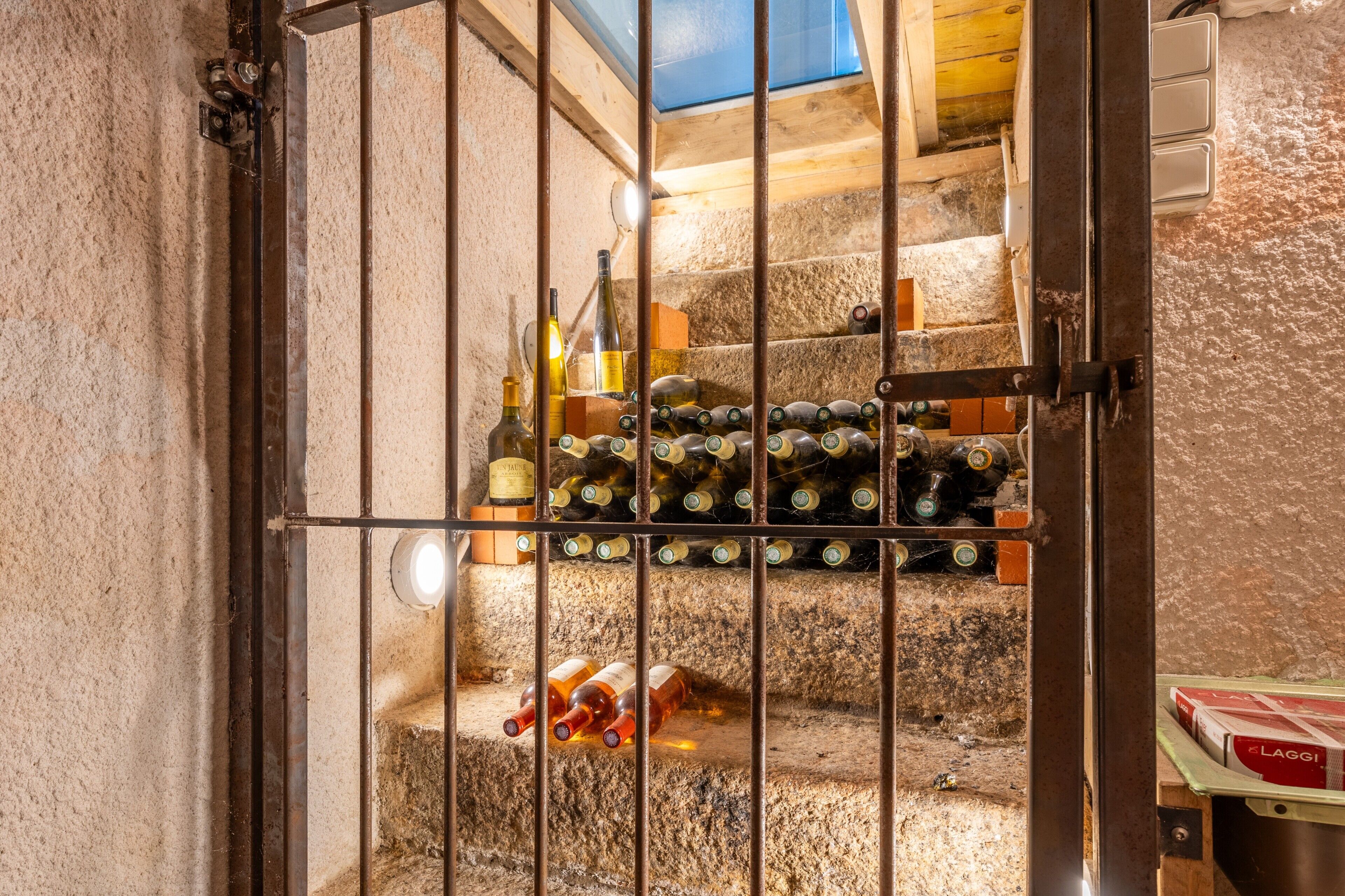 A wine cellar with a metal gate, bottles of wine, and a wooden staircase.