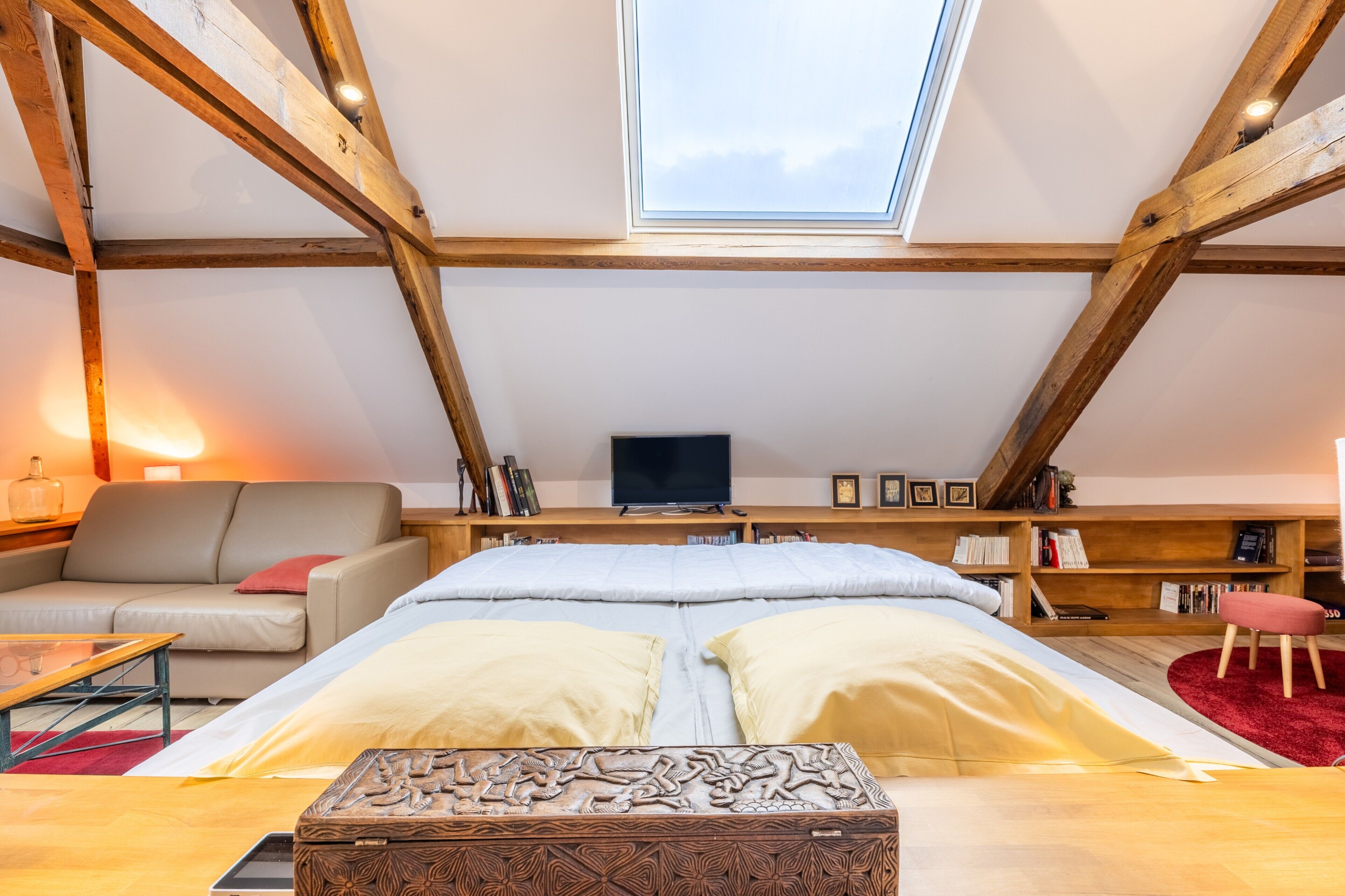 Une chambre avec un lit, une télévision, une bibliothèque et une lucarne.