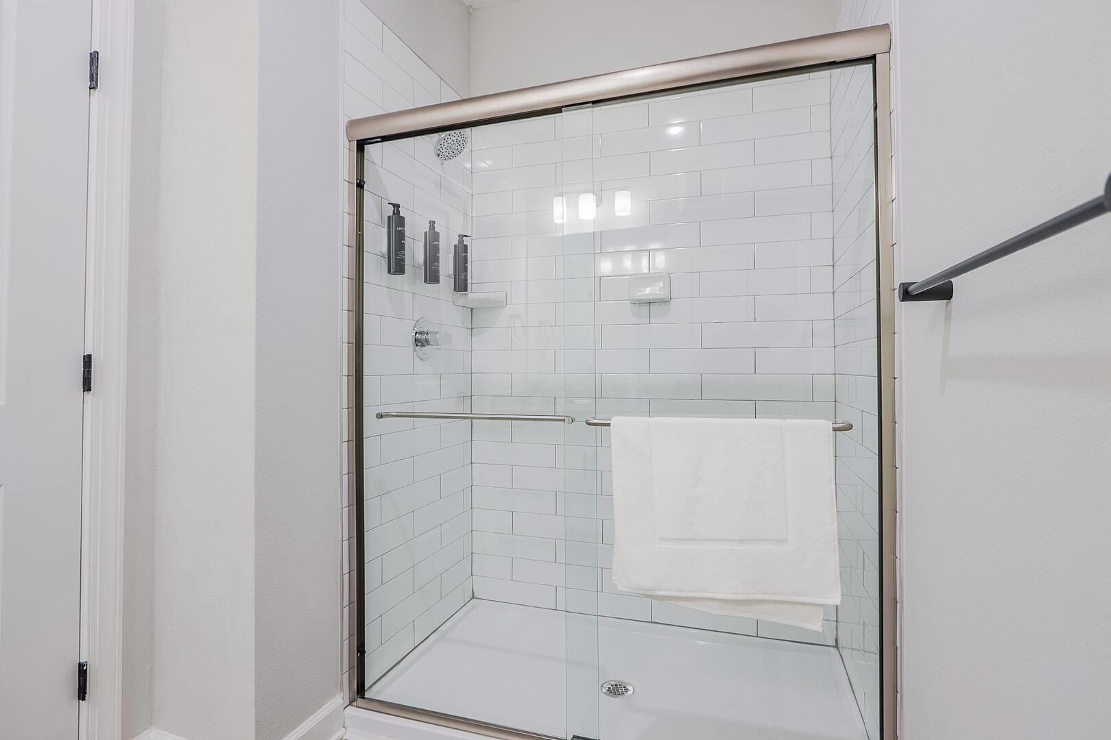 En dusch med glasväggar och vita kakelplattor på väggarna, en glasdörr och en handduksställning med ett vitt handduk.
