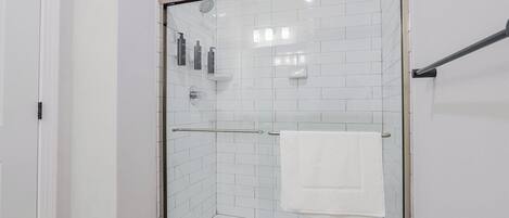 En dusch med glasväggar och vita kakelplattor på väggarna, en glasdörr och en handduksställning med ett vitt handduk.