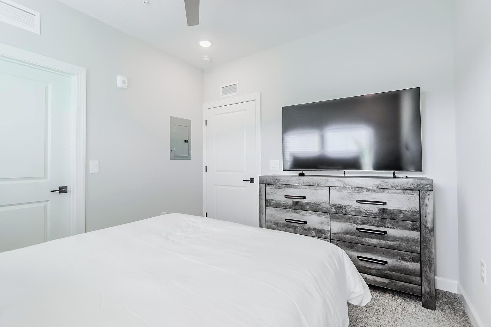A bedroom with a bed, a dresser, a television, and a door.