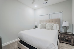 Quarto com uma cama, duas mesas de cabeceira, cabeceira e uma janela com persianas.