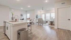 A modern kitchen with a central island, a dining area with a table and chairs, and a living space with a sofa and a TV. - Landing | Beautiful 2BD, Pool (Tice)