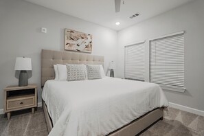 A bedroom with a large bed, two bedside tables with lamps, a ceiling fan, and a window with blinds. - Landing | Amazing 2BD, Gym, Pool (Tice)