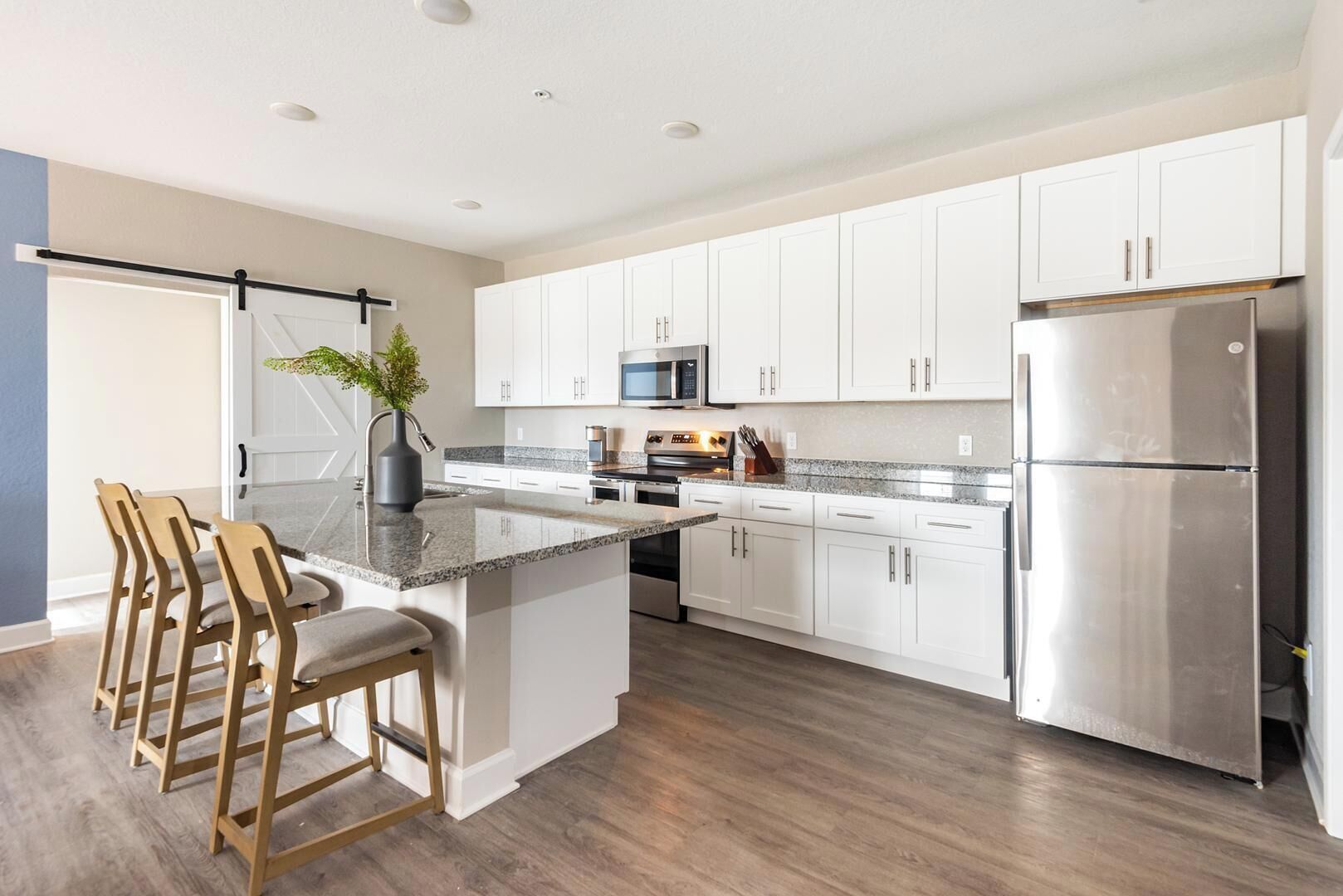 A modern kitchen with white cabinets, stainless steel appliances, and a wooden island with bar stools.