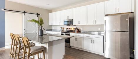 A modern kitchen with white cabinets, stainless steel appliances, and a wooden island with bar stools.