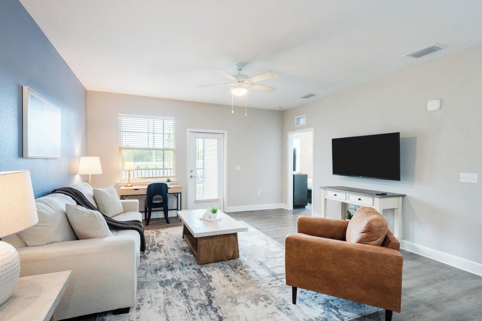 A living room with a sofa, armchair, coffee table, TV, and a ceiling fan.