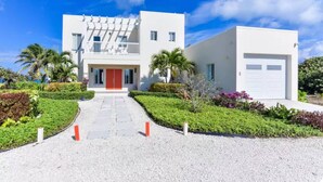 Un bâtiment moderne à deux étages, doté d’une porte rouge, d’un garage blanc et d’une allée gravillonnée.