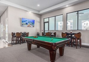Une table de billard dans une pièce dotée d’une grande fenêtre, de chaises et d’un tableau accroché au mur.