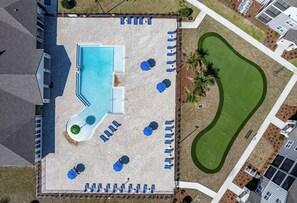 Vue aérienne d’un espace piscine comprenant une piscine rectangulaire, plusieurs chaises longues et un petit jardin.