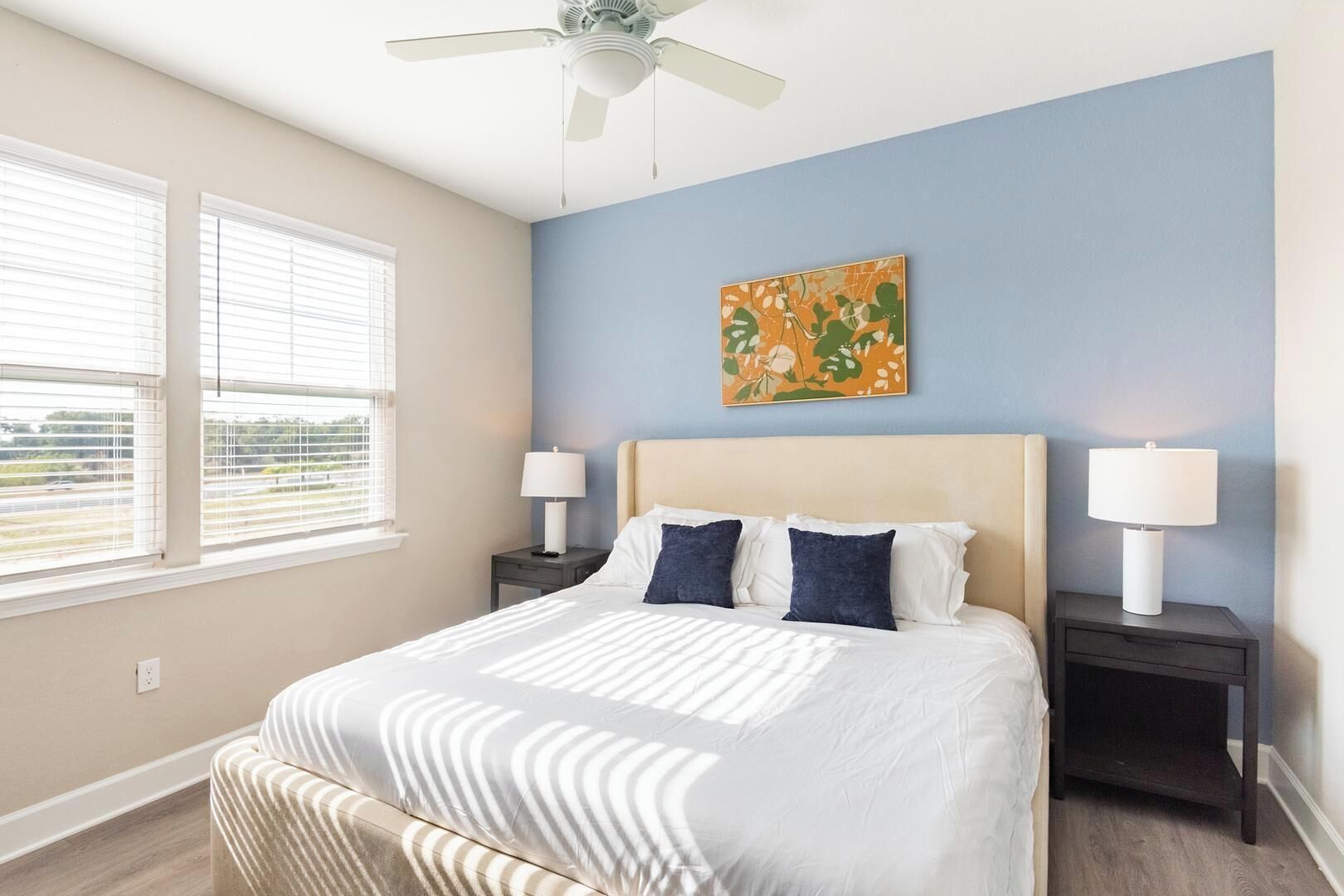 A bedroom with a bed, two bedside tables, a ceiling fan, and a window with blinds.