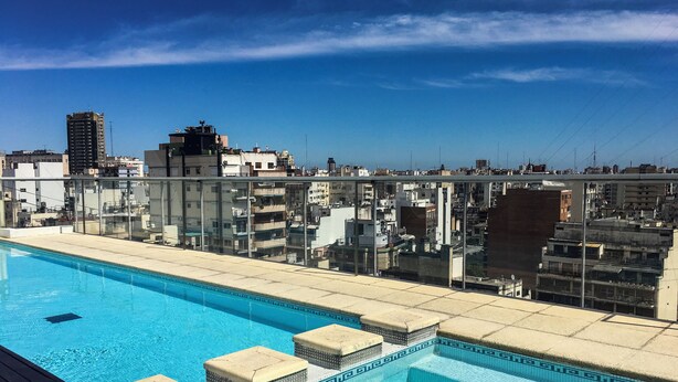 Ein Dachpool mit klarem, blauem Wasser, umgeben von Glasgeländern und mit Blick auf eine Stadtlandschaft mit verschiedenen Gebäuden.