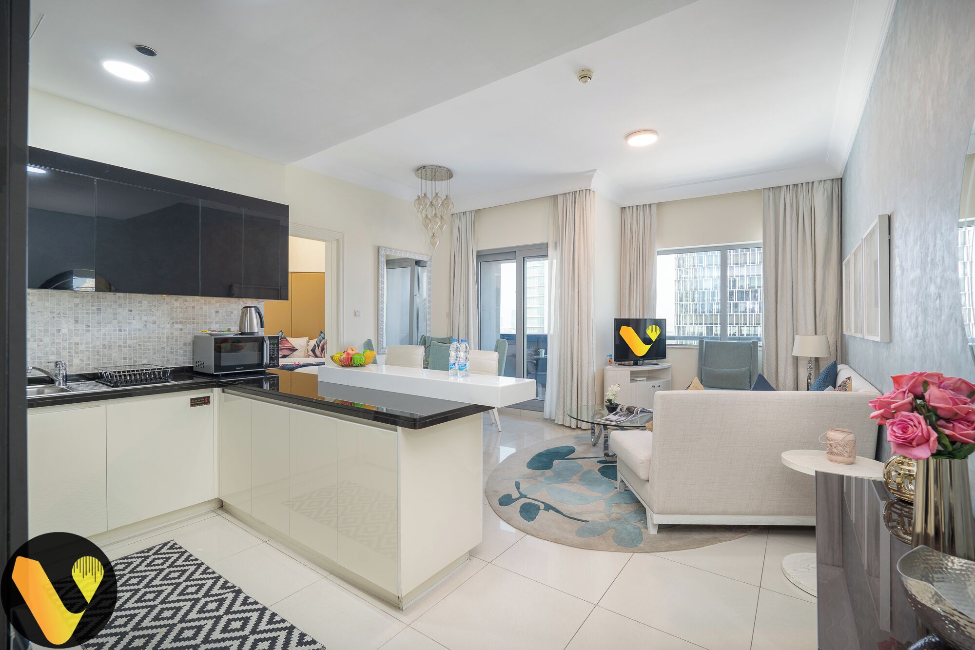A modern kitchen with a flat-screen TV, a dining area with a sofa, and a living room with a TV and a coffee table.