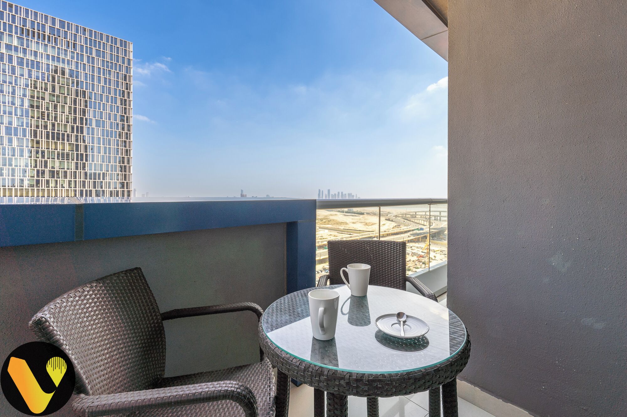 A balcony with a glass table, two wicker chairs, and a white mug.