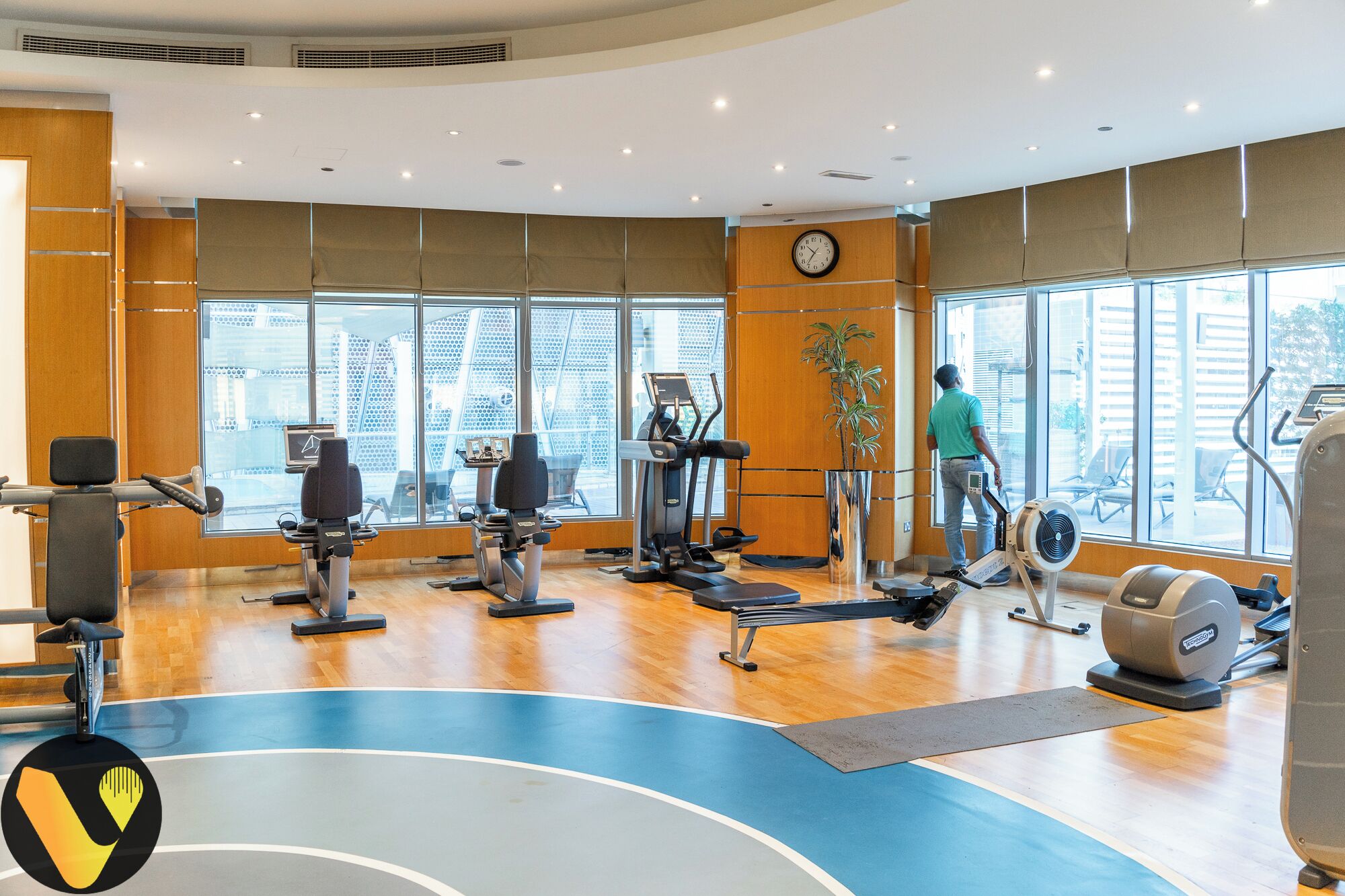 A gym with cardio machines, a large window, and a clock on the wall.