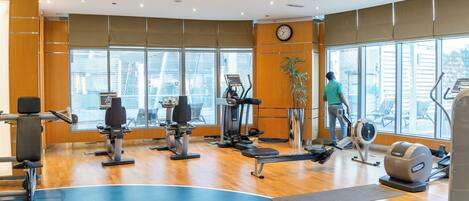A gym with cardio machines, a large window, and a clock on the wall.