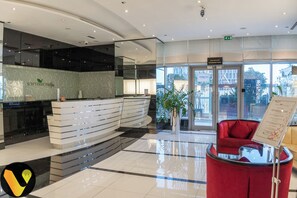 A modern reception area with a curved reception desk, a red seating area, and a glass door leading to a swimming pool. - Downtown near Dubai Mall Burj Khalifa (Dubai)