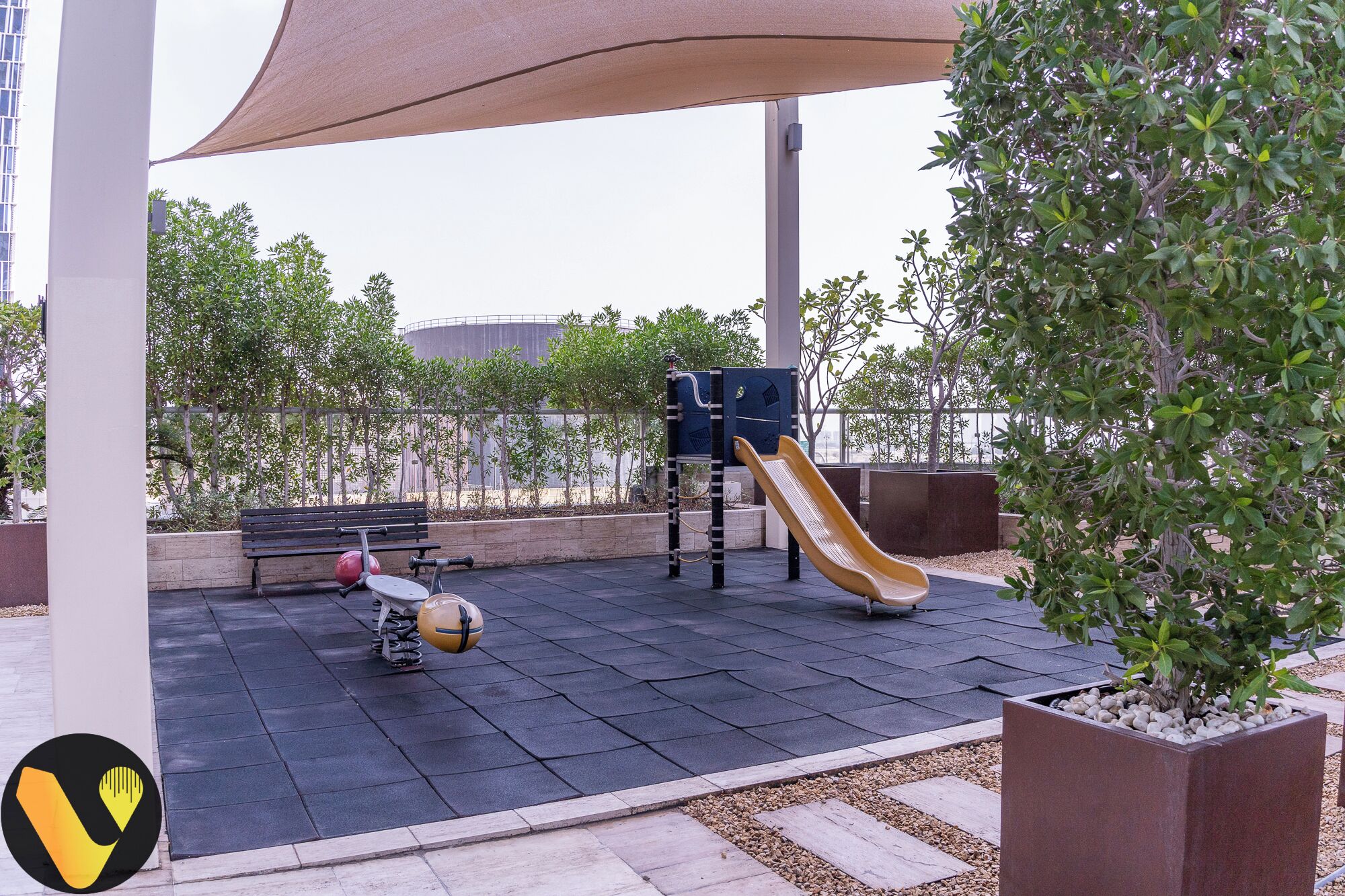 Ein Spielplatz mit Rutsche und Ball, umgeben von Bäumen und einer Bank.