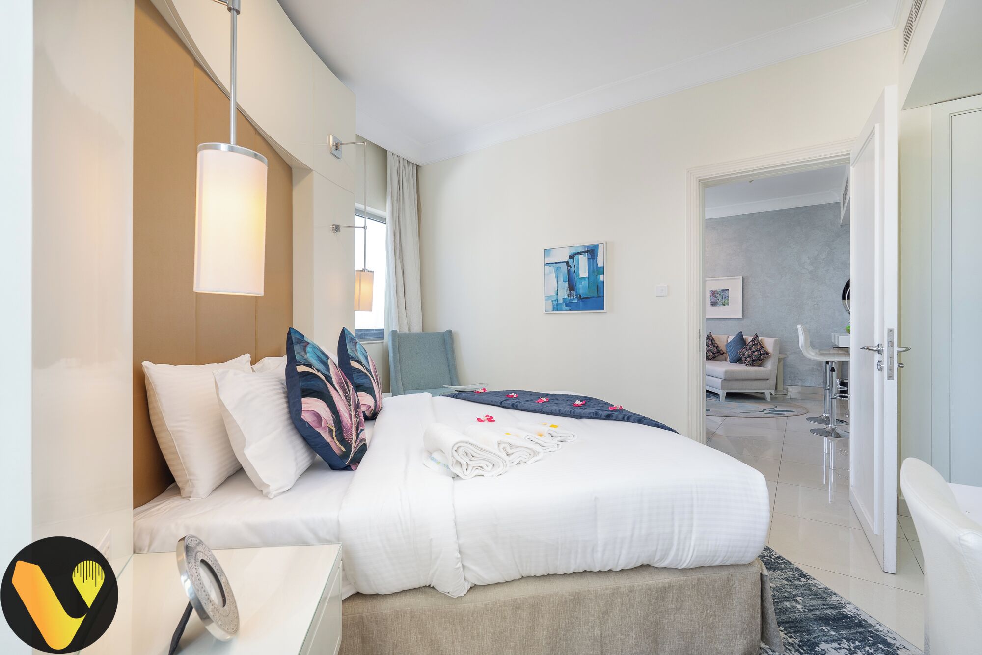 A modern hotel room with a bed, bedside table, lamp, artwork, and a view of the bathroom.