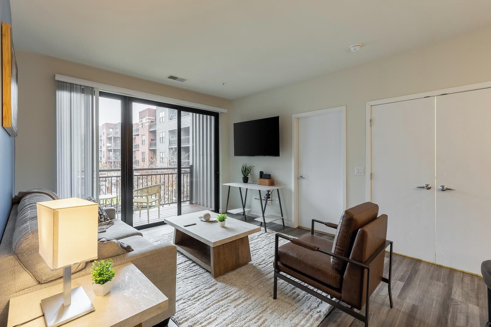 A modern living room with a sofa, a coffee table, a TV, and a balcony with a view of buildings.