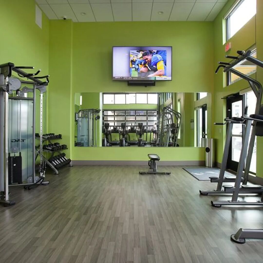 A gym with exercise equipment, a television mounted on the wall, and large windows.