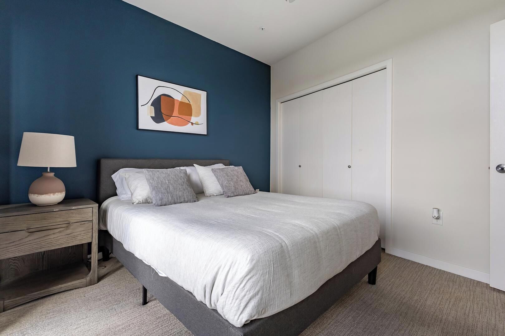 A bedroom with a bed, bedside table, lamp, and a door.