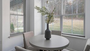 Et spiseområde med et rundt bord, fire stole og en vase med grene.