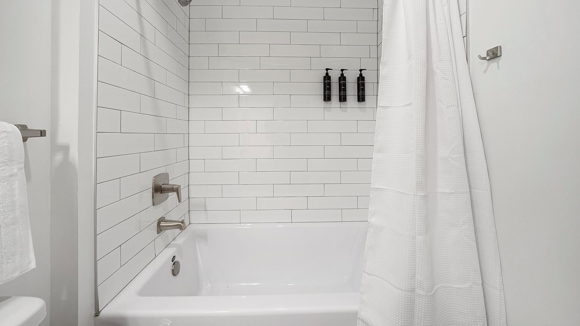 A modern bathroom with white tiled walls, a white bathtub, and a shower curtain.