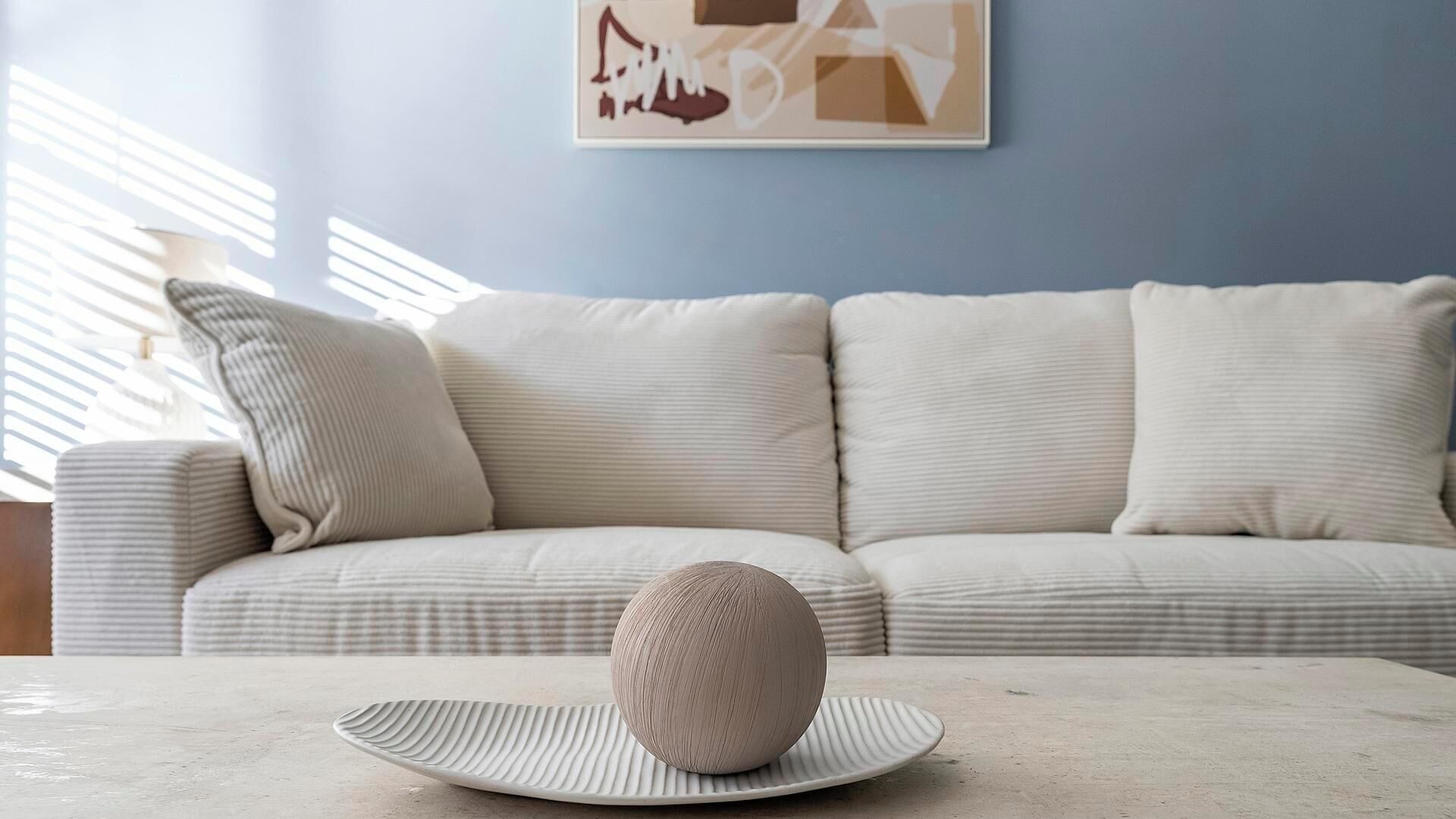 Un salon avec un canapé, une table ronde sur laquelle se trouve une assiette, et un mur orné d’un tableau encadré.