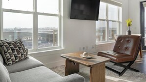 A modern living room with a grey sofa, a brown leather chair, a wooden coffee table, and a flat-screen TV mounted on the wall. - Landing | Beautiful 2BD, Yoga Studio, Game Room (Lawrenceville)
