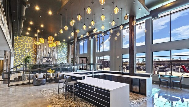 Eine geräumige Lobby mit einer zentralen Insellounge, großen Fenstern und hängenden Pendelleuchten.
