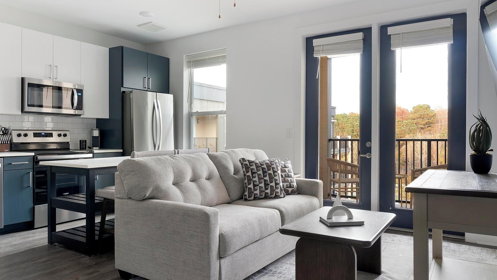 Eine moderne Wohnung mit einer Küchenzeile, einem grauen Sofa, einem Esstisch und einem Balkon mit Blick.