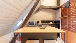 A compact kitchen with a wooden table, a black clock, and a microwave. - Studio Tess Apartment with Wi-Fi (Salies-de-Béarn)