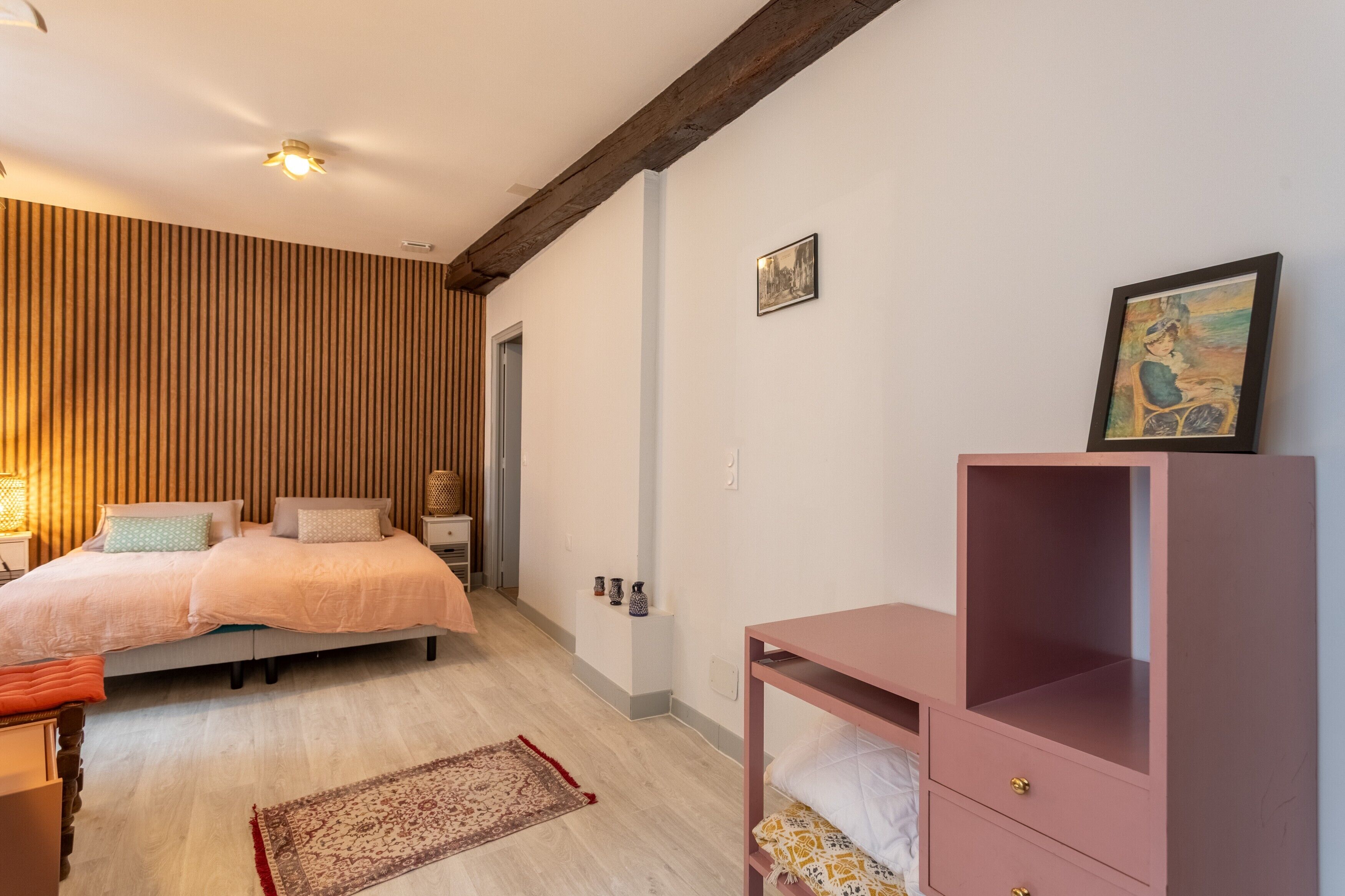 A bedroom with a bed, bedside tables, a dresser, a rug, and a wooden wall panel.