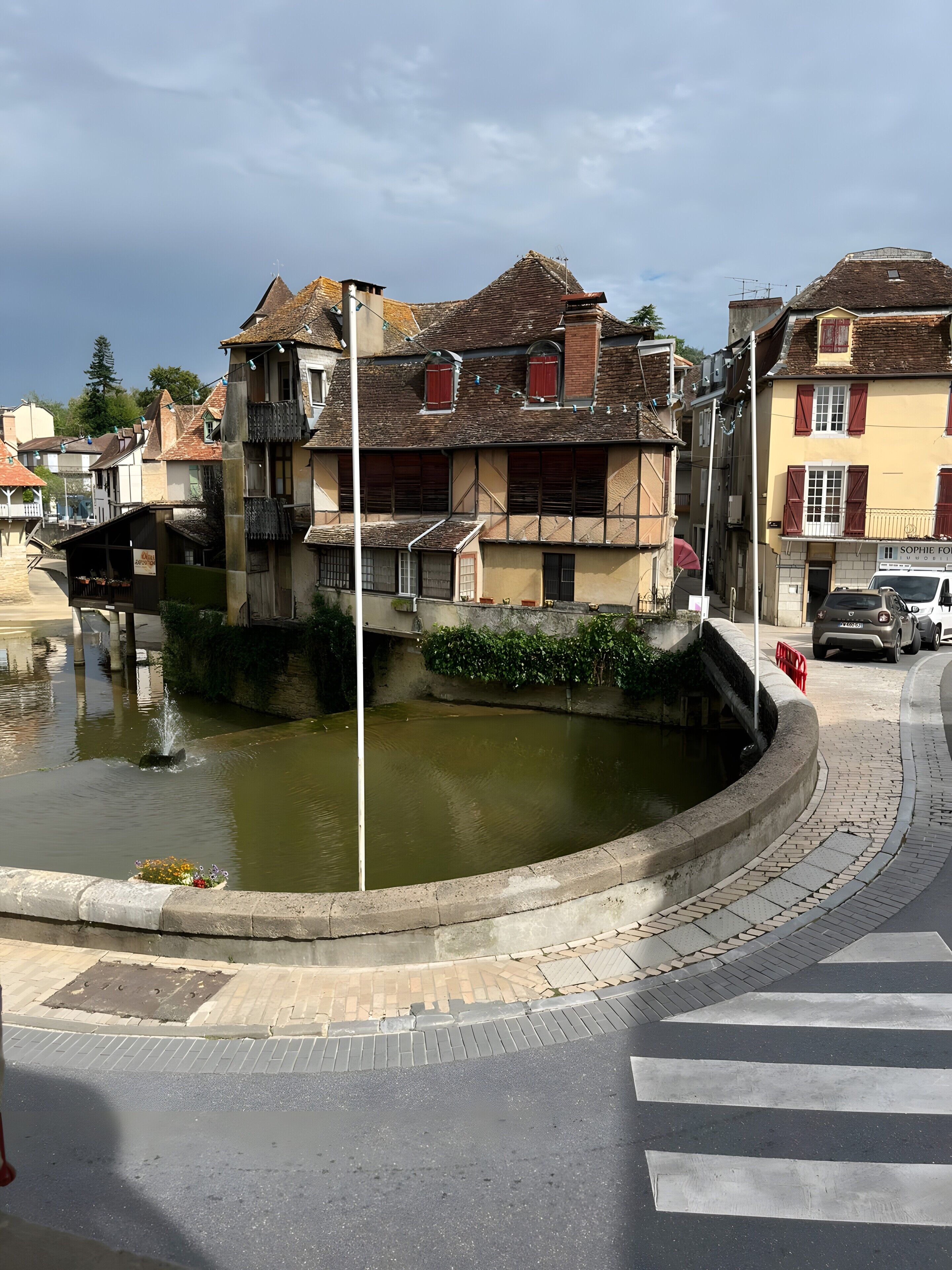 Un edificio con una fuente, un paso de peatones y una calle con coches estacionados.
