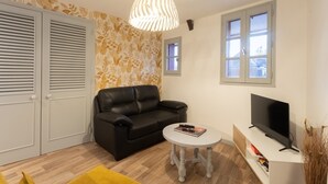 Ein Wohnzimmer mit einem schwarzen Ledersofa, einem weißen runden Tisch, einem Flachbildfernseher und einer Wand mit Muster.