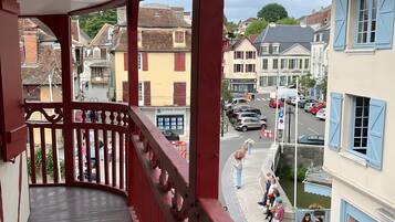 Un balcon avec une balustrade rouge donnant sur une rue bordée d’immeubles et de voitures garées.
