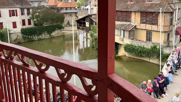 Ein Balkon mit roter Brüstung blickt auf eine Stadt mit historischen Gebäuden und einem Kanal.