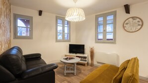 Ein Wohnzimmer mit einer Couch, einem Tisch, einem Fernseher und einem Fenster.