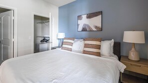 A hotel room with a large bed, a wardrobe, a bedside table with a lamp, and a wall-mounted picture. - Landing | Amazing 1BD, Gym, Clubhouse (Houston)