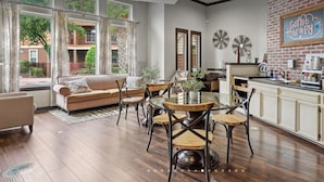 Ein modernes Wohnzimmer mit einer Couch, einem Esstisch und Stühlen. Es gibt eine Küchenzeile mit einer Kaffeestation und Blick ins Freie.