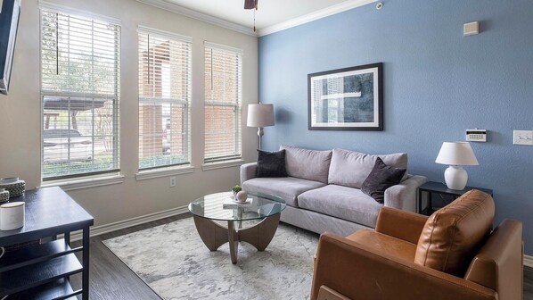 A living room with a sofa, two side tables, a glass coffee table, and a view through large windows. - Landing | Amazing 1BD, Gym, Clubhouse (Houston)