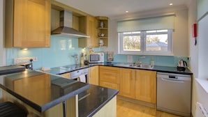 A modern kitchen with wooden cabinets, a black countertop, a microwave, a sink, and a dishwasher. - No 8 The Links Apartment Brora (Brora)