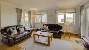 A living room with two brown leather sofas, a wooden coffee table, and a small side table with a lamp. - No 8 The Links Apartment Brora (Brora)