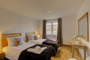 Quarto de hotel com duas camas, uma escrivaninha de madeira e uma janela com cortinas.