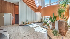 Eine geräumige Lobby mit hoher Decke, einer zentralen Treppe und verschiedenen Pflanzen, darunter Kakteen.