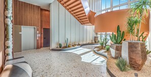 A spacious lobby with a high ceiling, a central staircase, and a variety of plants including cacti. - Landing | Chic 1BD, Gym, Pool (Enterprise)